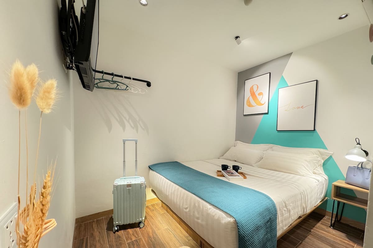 Una habitación de hotel moderna con una cama, una maleta, un escritorio con lámpara y una obra de arte en la pared.