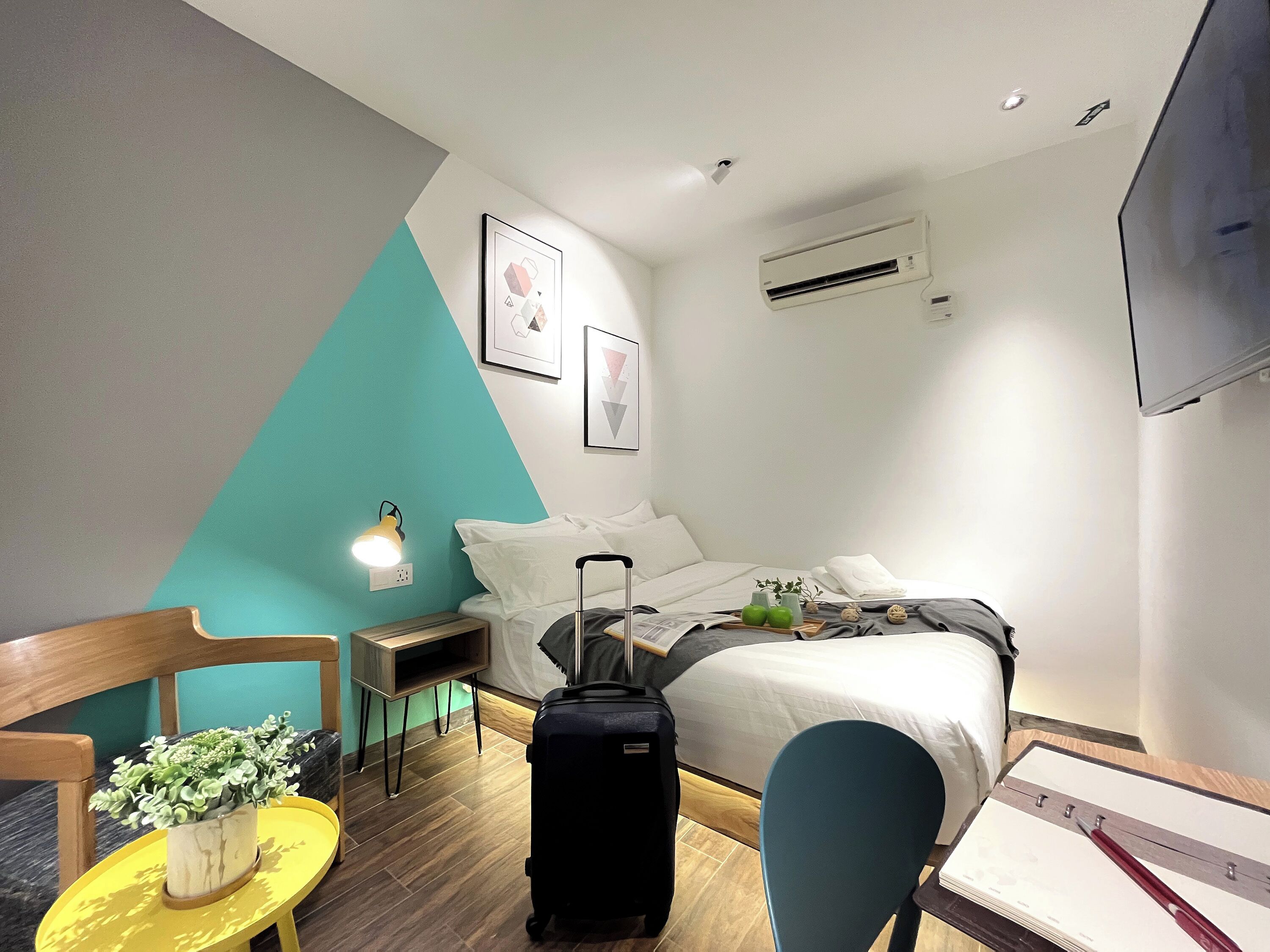 A hotel room with a bed, a desk, a chair, a suitcase, and a TV.