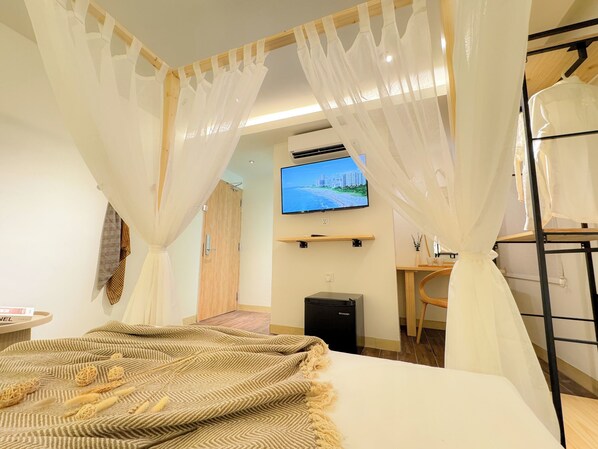 A hotel room with a bed, a TV mounted on the wall, a desk, and a bunk bed. - Apple 1 Hotel Queensbay (George Town)