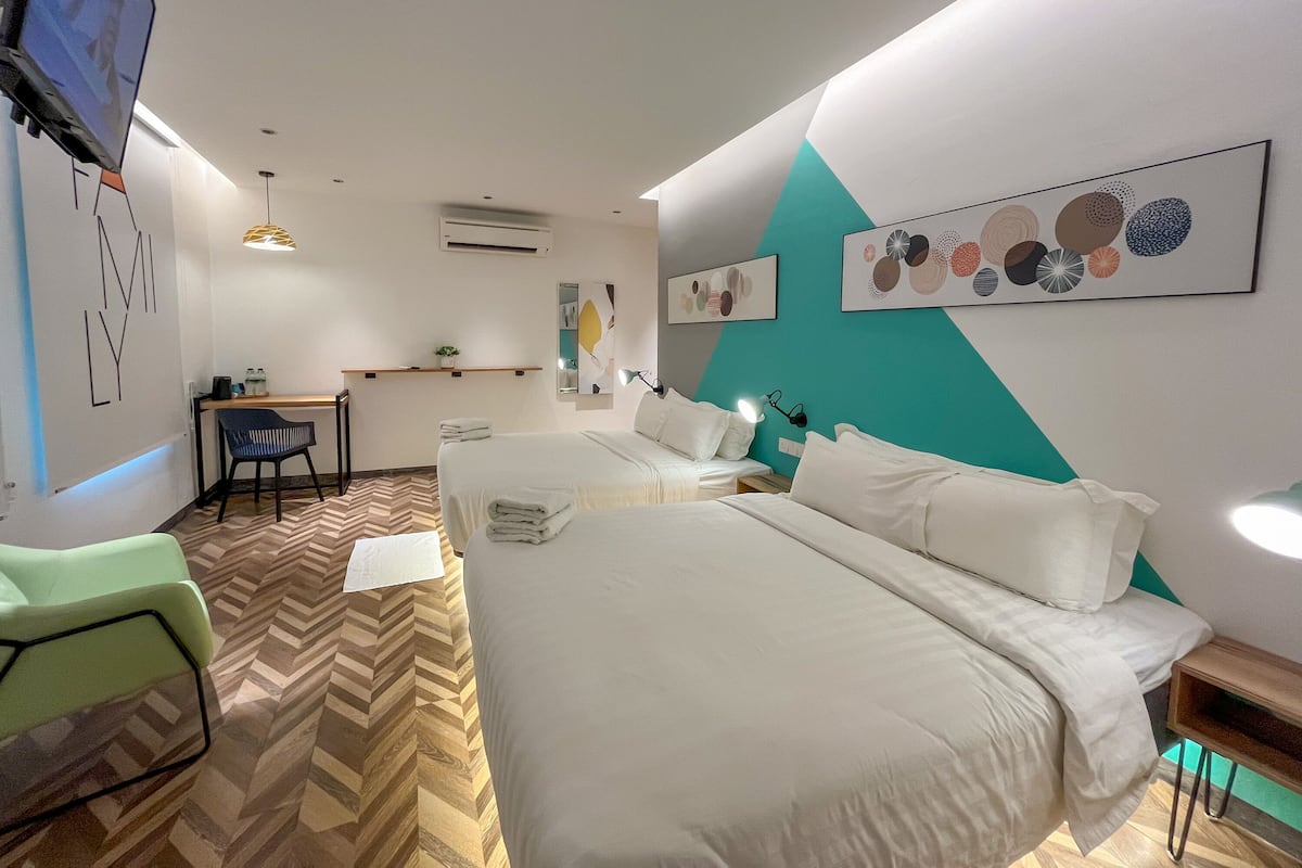 Habitación de hotel con dos camas, un escritorio, una silla y obras de arte en las paredes.