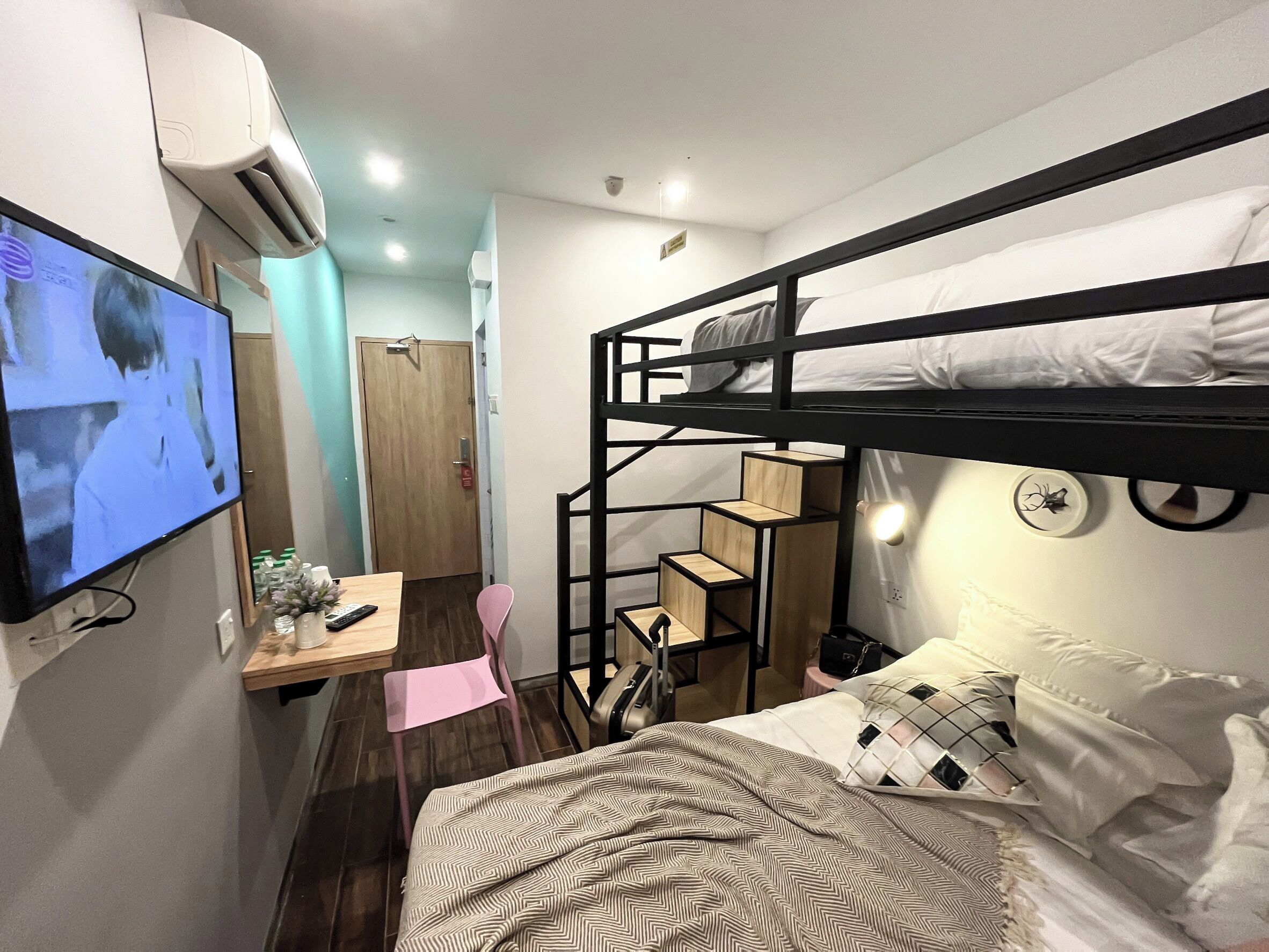 Une chambre d’hôtel compacte avec des lits superposés, un bureau avec une chaise, une télévision et une petite kitchenette.
