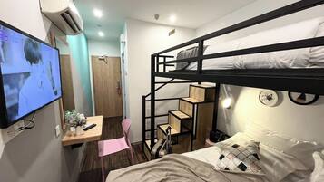 Une chambre d’hôtel compacte avec des lits superposés, un bureau avec une chaise, une télévision et une petite kitchenette.