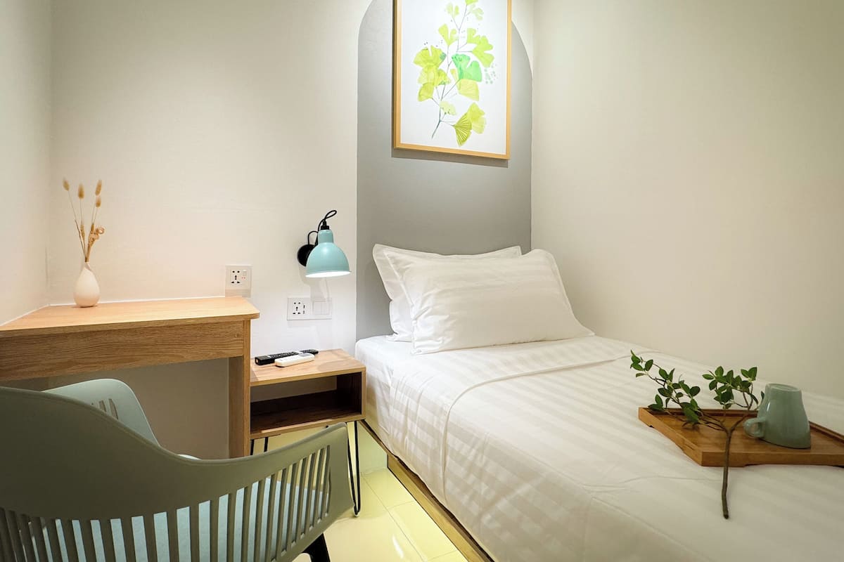 Un dormitorio con cama, mesita de noche, lámpara, silla y una obra de arte en la pared.
