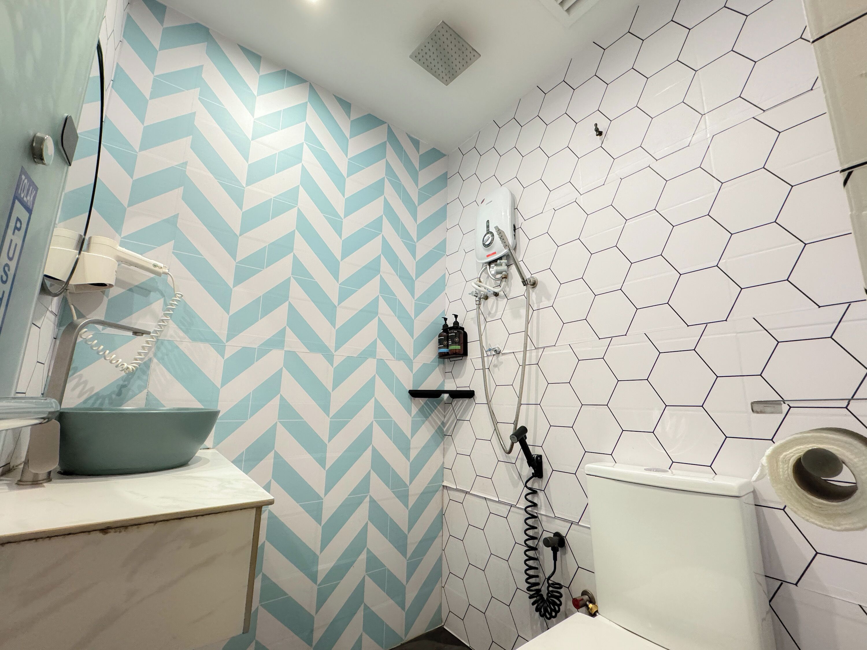 Een badkamer met een zigzaagmozaïek muur, een wit toilet, een douche met een slangdouche en een wastafel.