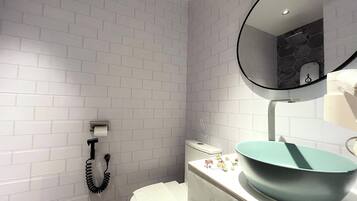 Une salle de bain avec des murs recouverts de carreaux blancs, des toilettes, un lavabo doté d’un grand bac et un miroir avec un pare-éclaboussures en forme d’hexagone.