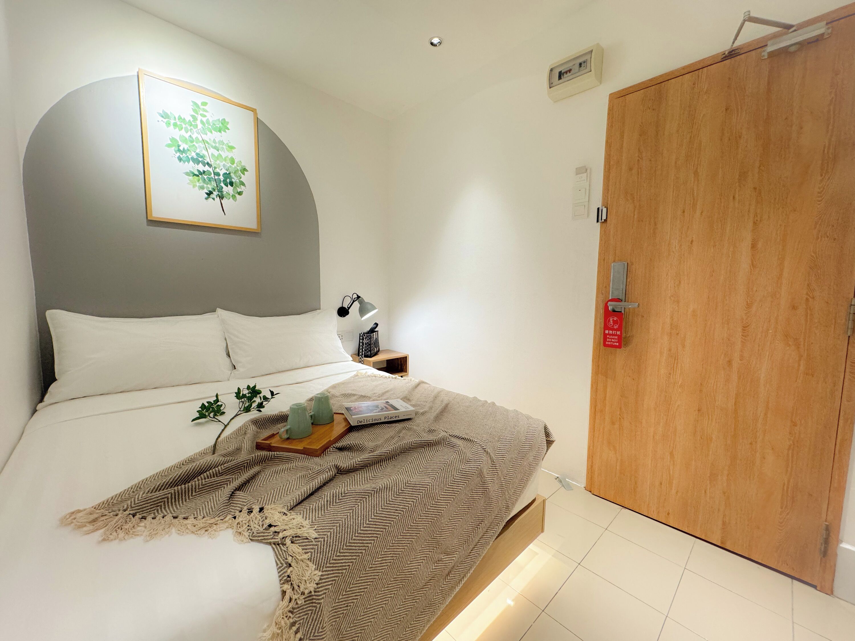 A neatly made bed with a herringbone throw blanket, a bedside table with a lamp, and a framed picture on the wall.