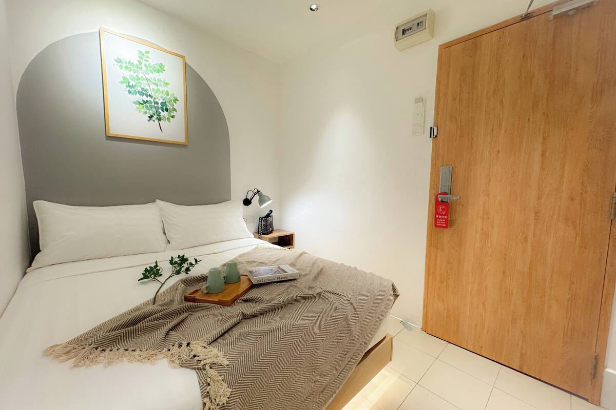 A neatly made bed with a herringbone throw blanket, a bedside table with a lamp, and a framed picture on the wall.