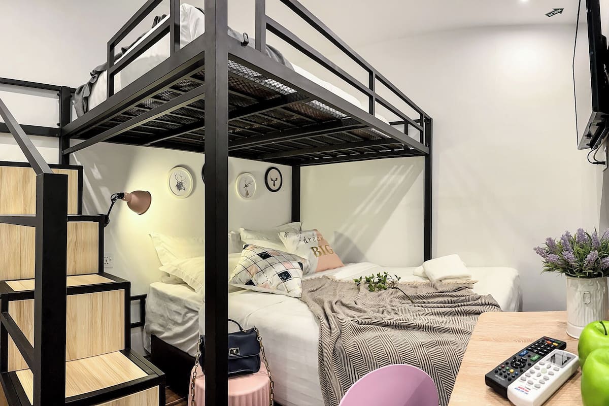 Habitación con literas, un escritorio, una silla, un control remoto, manzanas verdes, botellas de agua y un florero con flores.