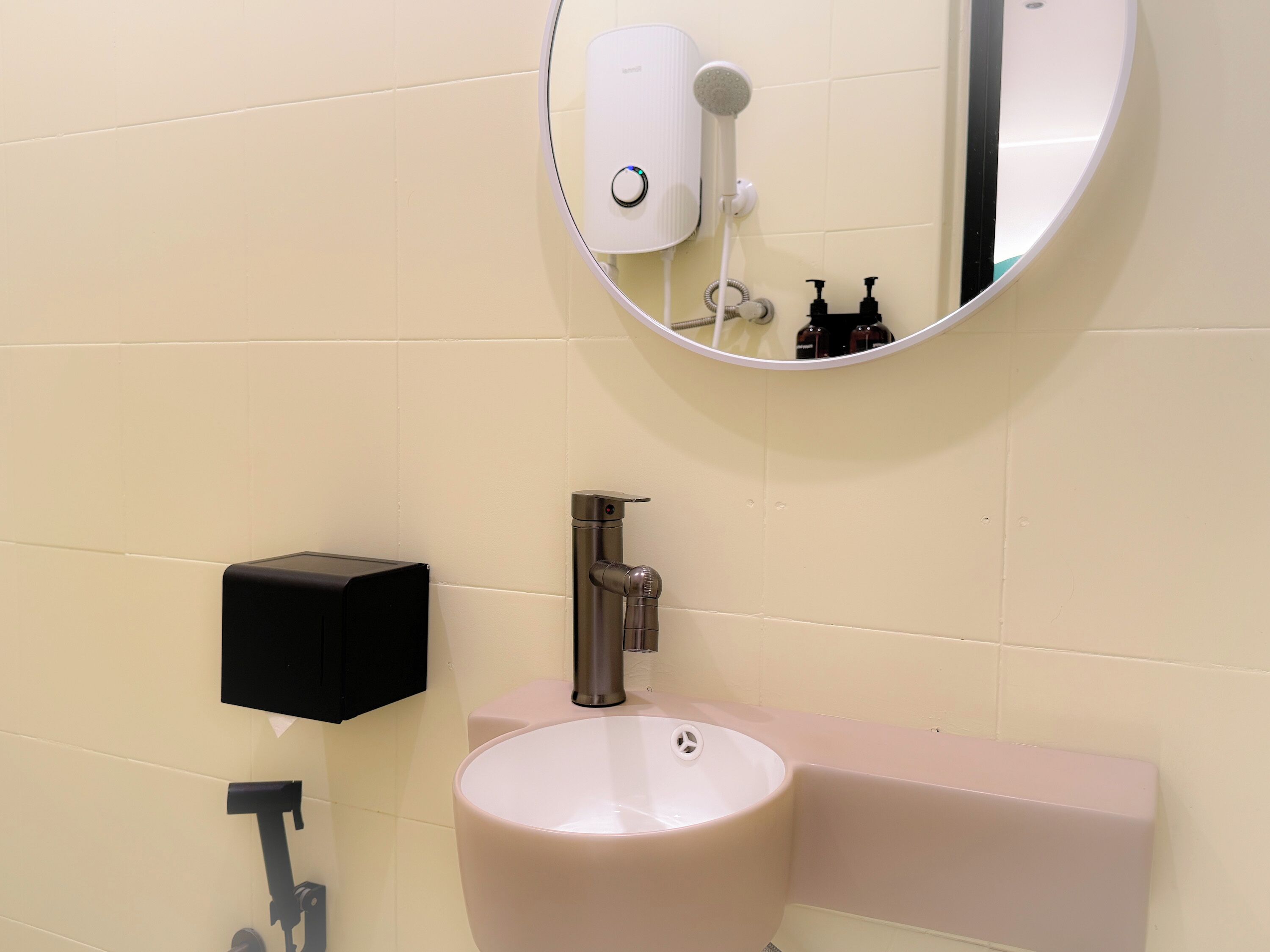 A bathroom with a round mirror, a sink, and a soap dispenser.
