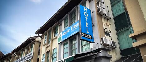 A hotel with a prominent 'Apple 1 Hotel' sign, multiple air conditioning units, and a 'Law & Chew' sign below.