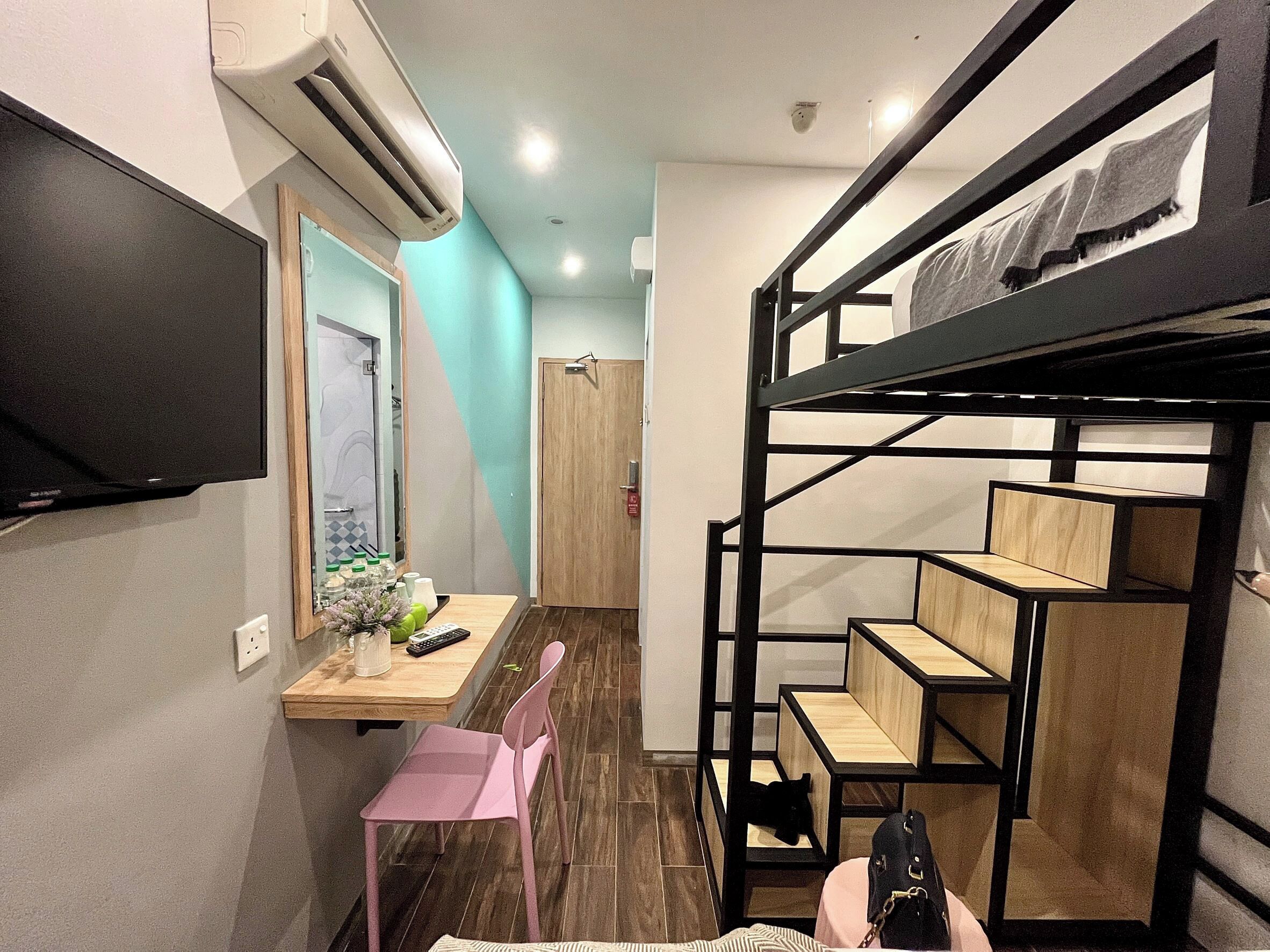 A compact room with a bunk bed, a small desk with a chair, a TV mounted on the wall, and an air conditioning unit.