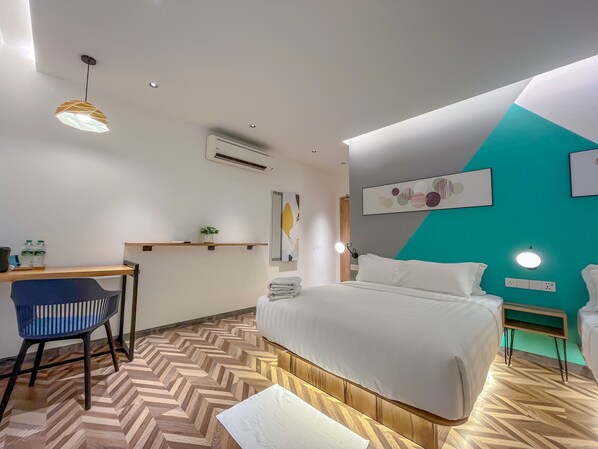 Une chambre d’hôtel moderne avec un grand lit, un bureau avec une chaise, une petite table avec une plante et une étagère fixée au mur.
