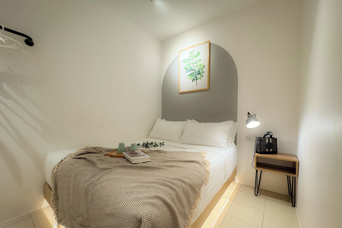 Un dormitorio ordenado con cama, mesita de noche, lámpara y un cuadro en la pared.
