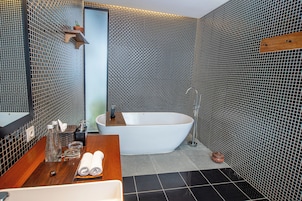 Un baño moderno con una bañera independiente, un tocador de madera con espejo y suelo de baldosas.