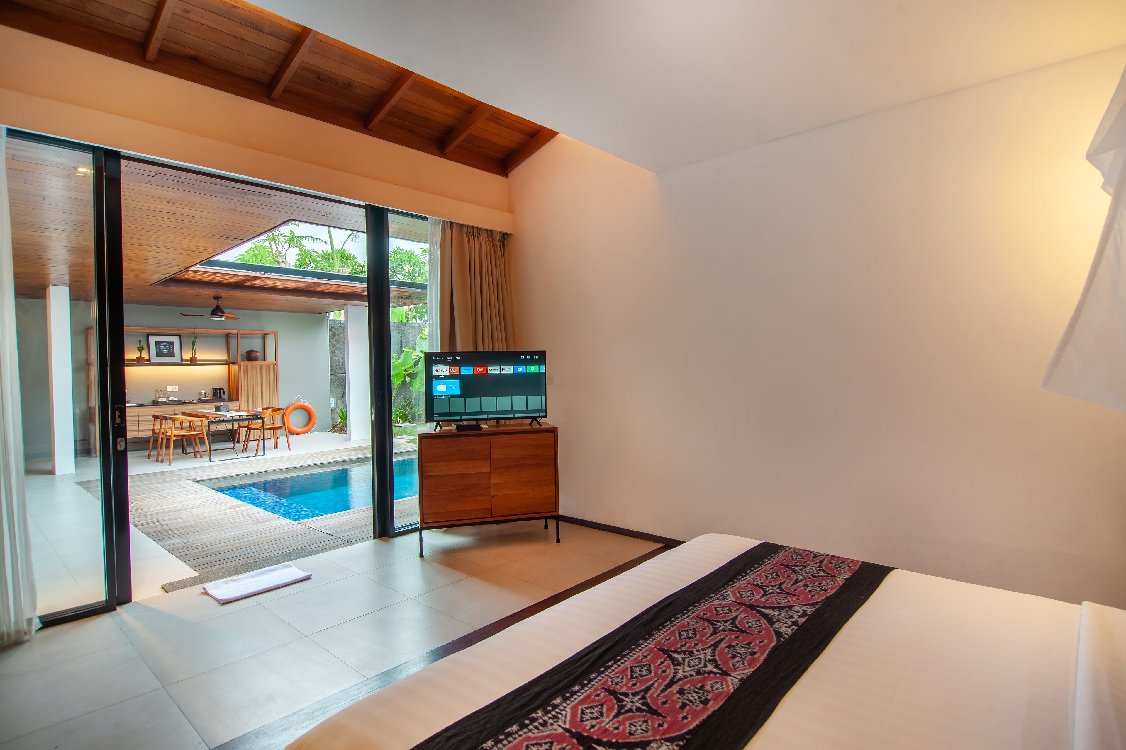 A modern hotel room with a large bed, a television, and a view of a pool and outdoor dining area.