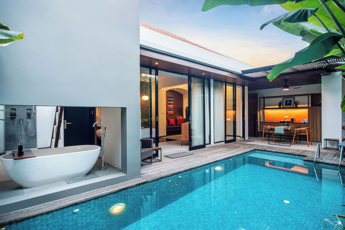 A modern outdoor pool area with a freestanding bathtub, a dining area with a table and chairs, and a cozy seating area with cushions.