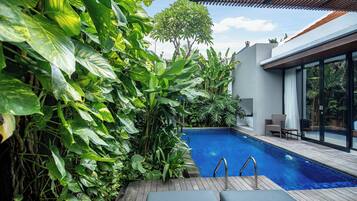 A modern outdoor pool area with lush greenery, a wooden deck, and a seating area with a view of the pool.