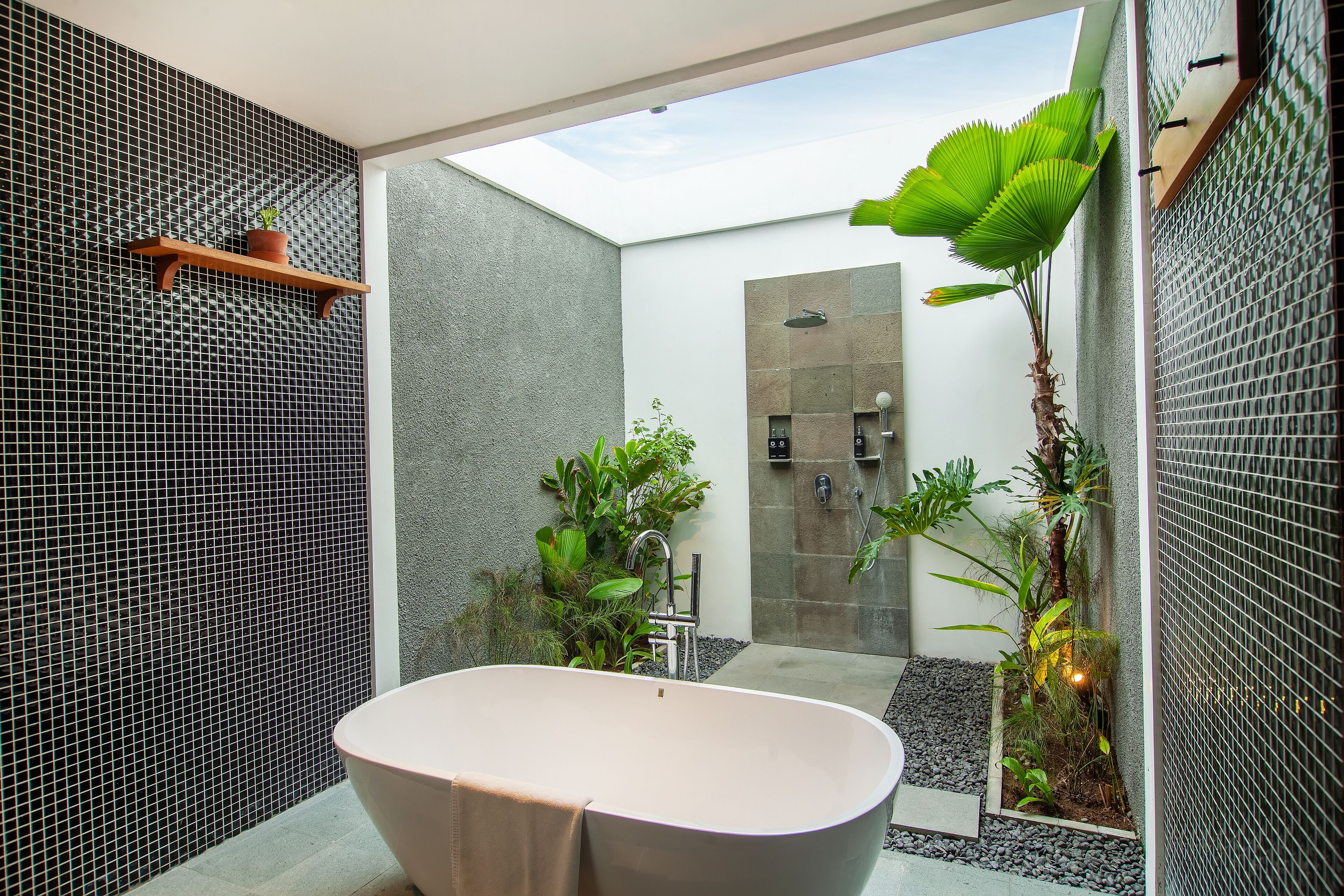A modern bathroom with a freestanding bathtub, a shower area, and a small garden with plants.