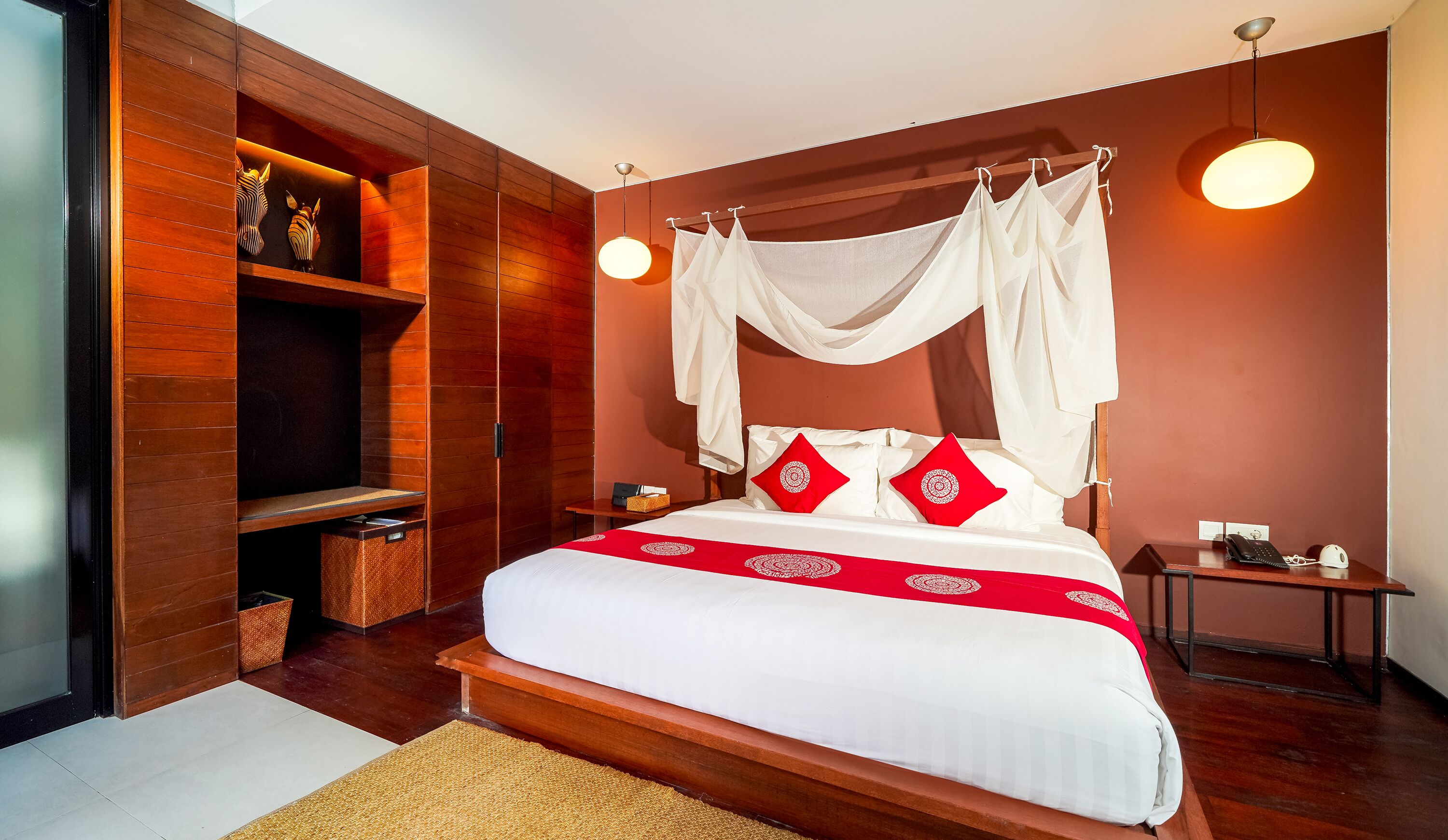 A bedroom with a canopy bed, a bedside table with a lamp, a bedside phone, and a wall-mounted shelf.