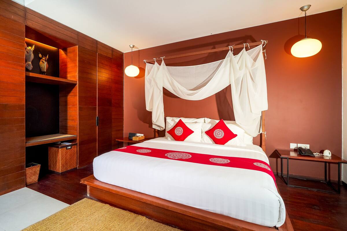 A bedroom with a canopy bed, a bedside table with a lamp, a bedside phone, and a wall-mounted shelf.