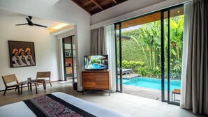A hotel room with a large bed, a television, a dining area, and a view of a swimming pool. - Abia Villa and Suite Legian (Legian)