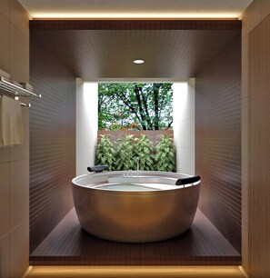 Une salle de bain moderne avec une grande baignoire ronde, un porte-serviettes et une vue sur la verdure à l’extérieur.