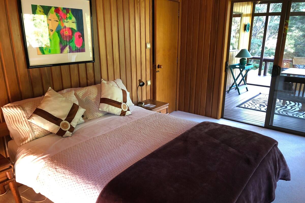 Un dormitorio con una cama grande, paneles de madera, una obra de arte enmarcada y vistas a una terraza exterior.