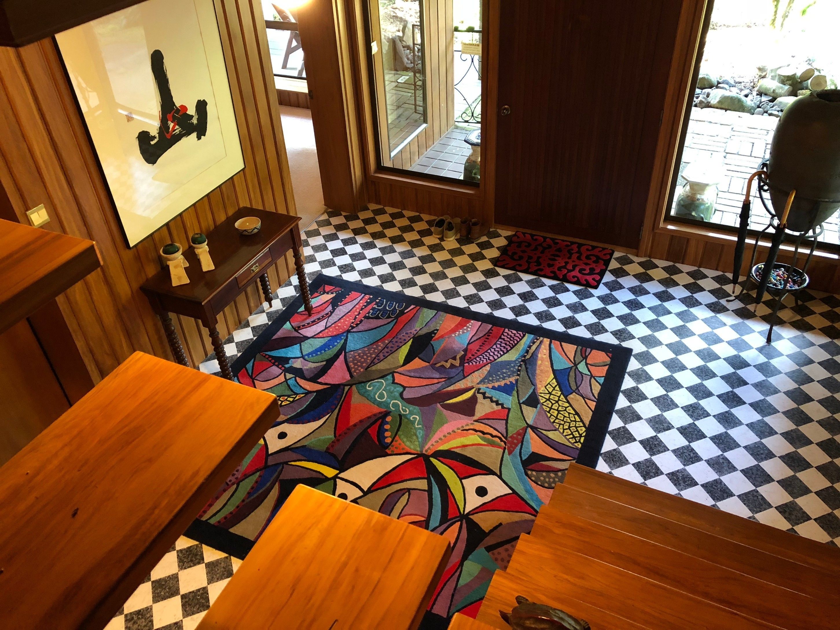 Una habitación con suelo a cuadros, alfombra colorida, muebles de madera y vistas al exterior.