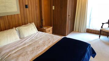 A bedroom with a bed, a nightstand, a wooden wardrobe, a chair, and a window with curtains.