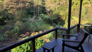 Una terraza de madera con bancos que da a un jardín exuberante y una ladera boscosa.