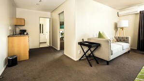 A hotel room with a sofa, a small table, a lamp, a trash bin, and a kitchenette area. - Edit Auckland Greenlane (Auckland)