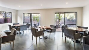 A modern dining area with multiple tables and chairs, large windows with plants, and a clean, contemporary design. - Edit Auckland Greenlane (Auckland)