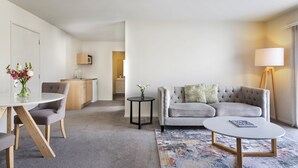 A modern living room with a grey sofa, a round coffee table, and a dining area with a table and chairs. - Edit Auckland Greenlane (Auckland)