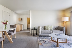 A modern living room with a grey sofa, a round coffee table, and a dining area with a table and chairs.