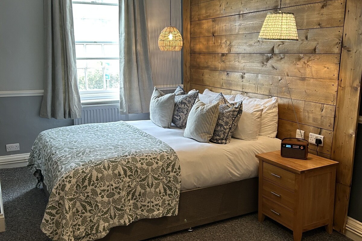 A bedroom with a large bed, a wooden headboard, a bedside table with a radio, and a window with curtains.