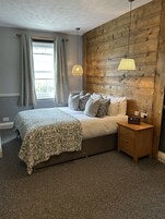 A bedroom with a large bed, a wooden headboard, a bedside table with a radio, and a window with curtains.