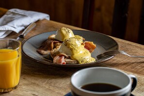 A breakfast plate with eggs, bacon, and hollandaise sauce, accompanied by a glass of orange juice and a cup of coffee on a wooden table. - The Pelican Inn (Marlborough)