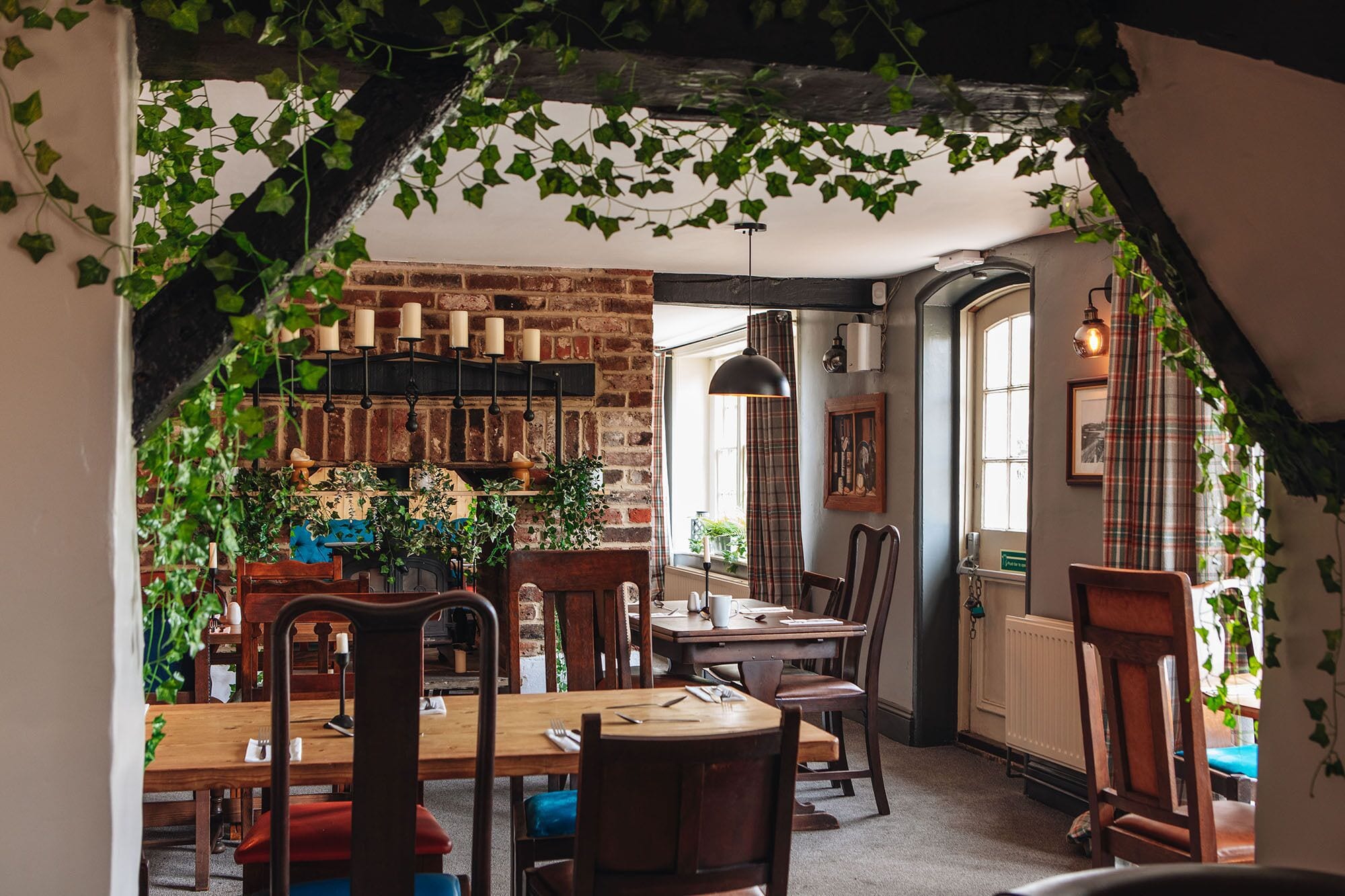 A cozy dining area with brick walls, wooden furniture, and hanging plants.