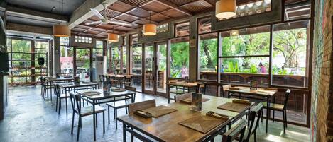 A spacious restaurant with high ceilings, large windows, and wooden tables and chairs.