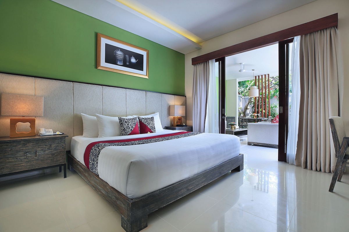 Habitación de hotel con una cama grande, una mesita de noche con lámpara, un cuadro en la pared y vistas al exterior.