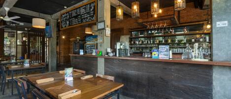 Ein Restaurant mit Holztischen und -stühlen, einer Bar mit Flaschenregalen sowie hängenden Pendelleuchten.