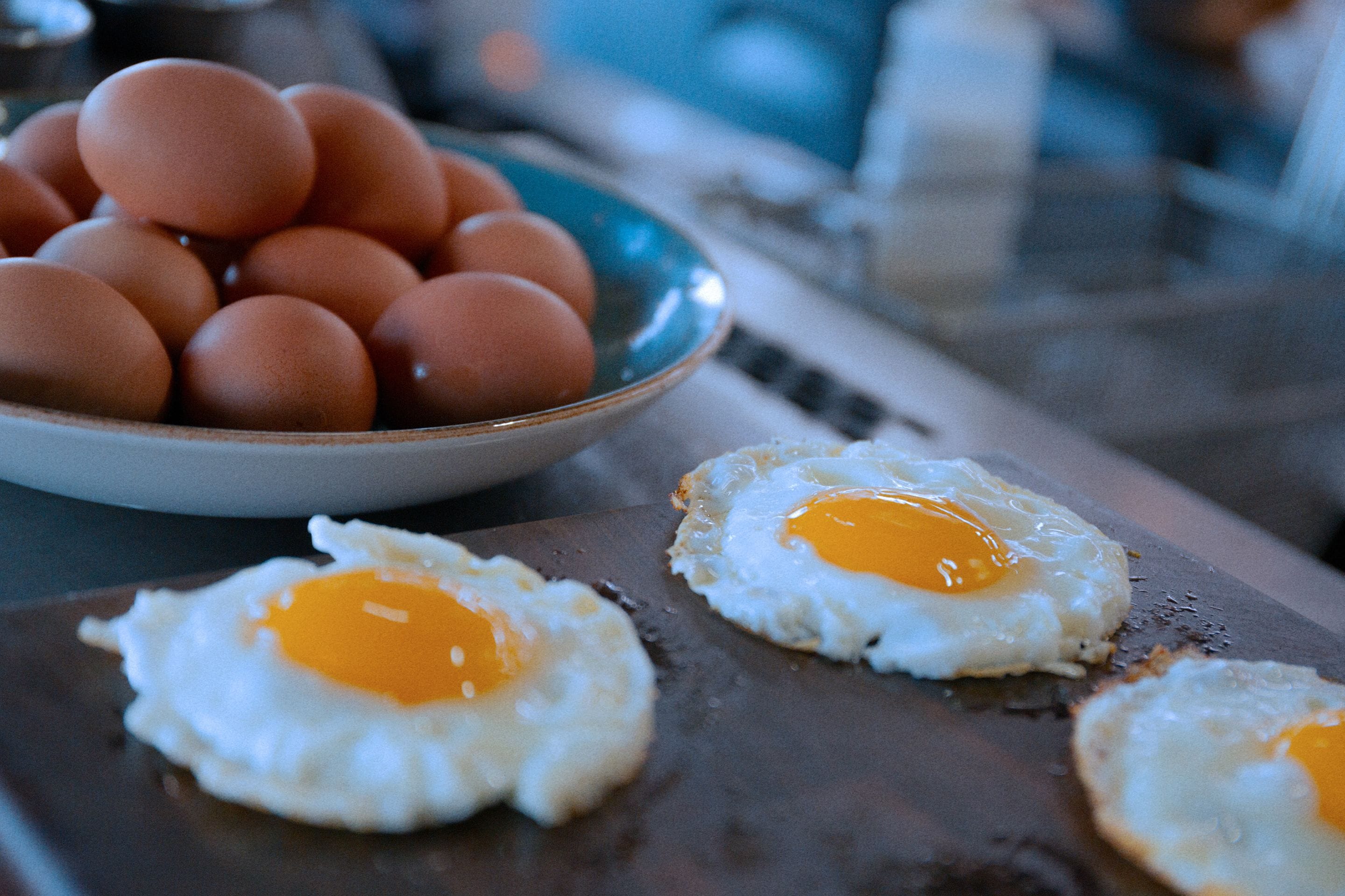 A plate with three sunny-side-up eggs and a bowl of eggs in the background.