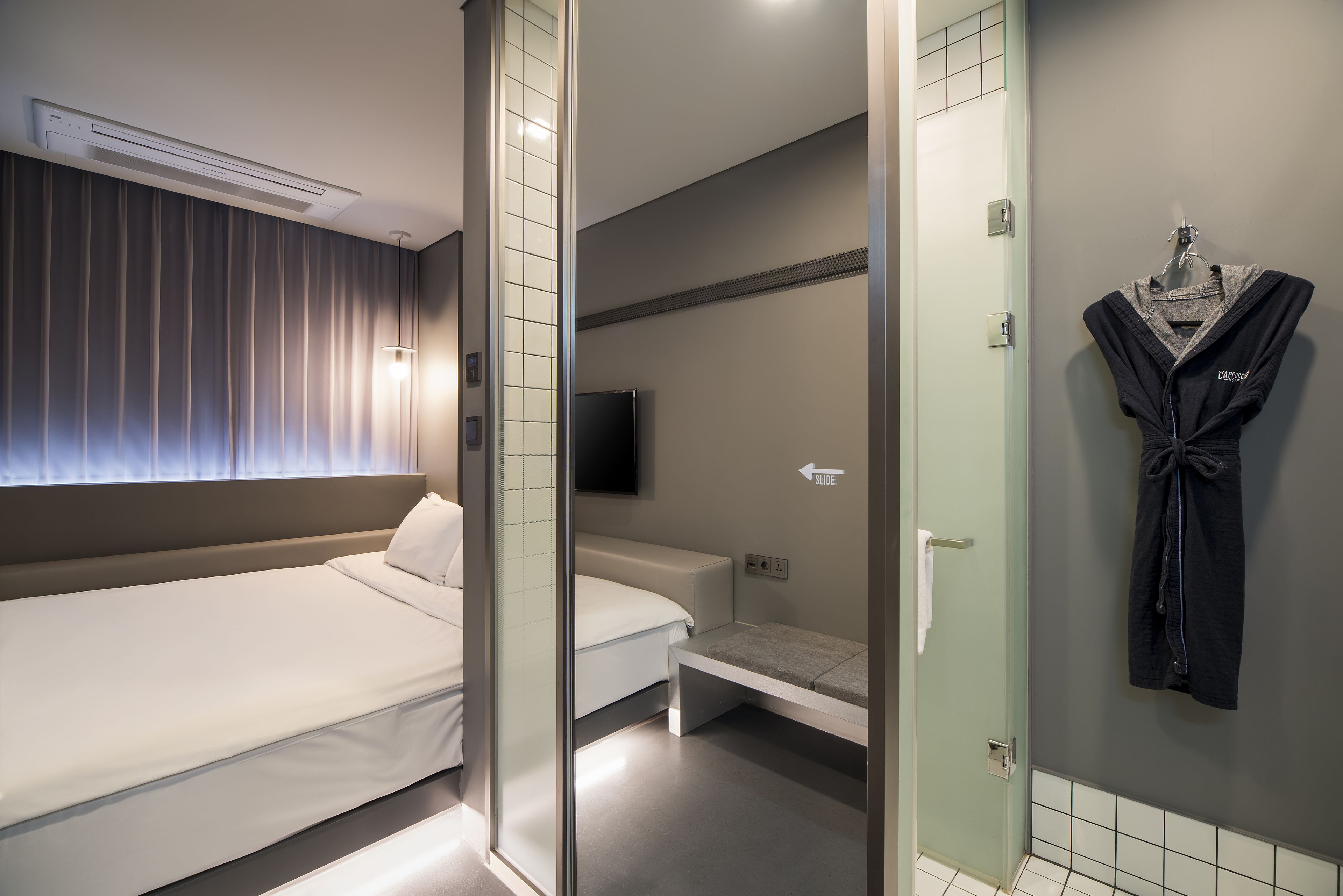 Una habitación de hotel moderna con una cama grande, una cama más pequeña, una zona de estar, un televisor y una bata colgada en la pared.