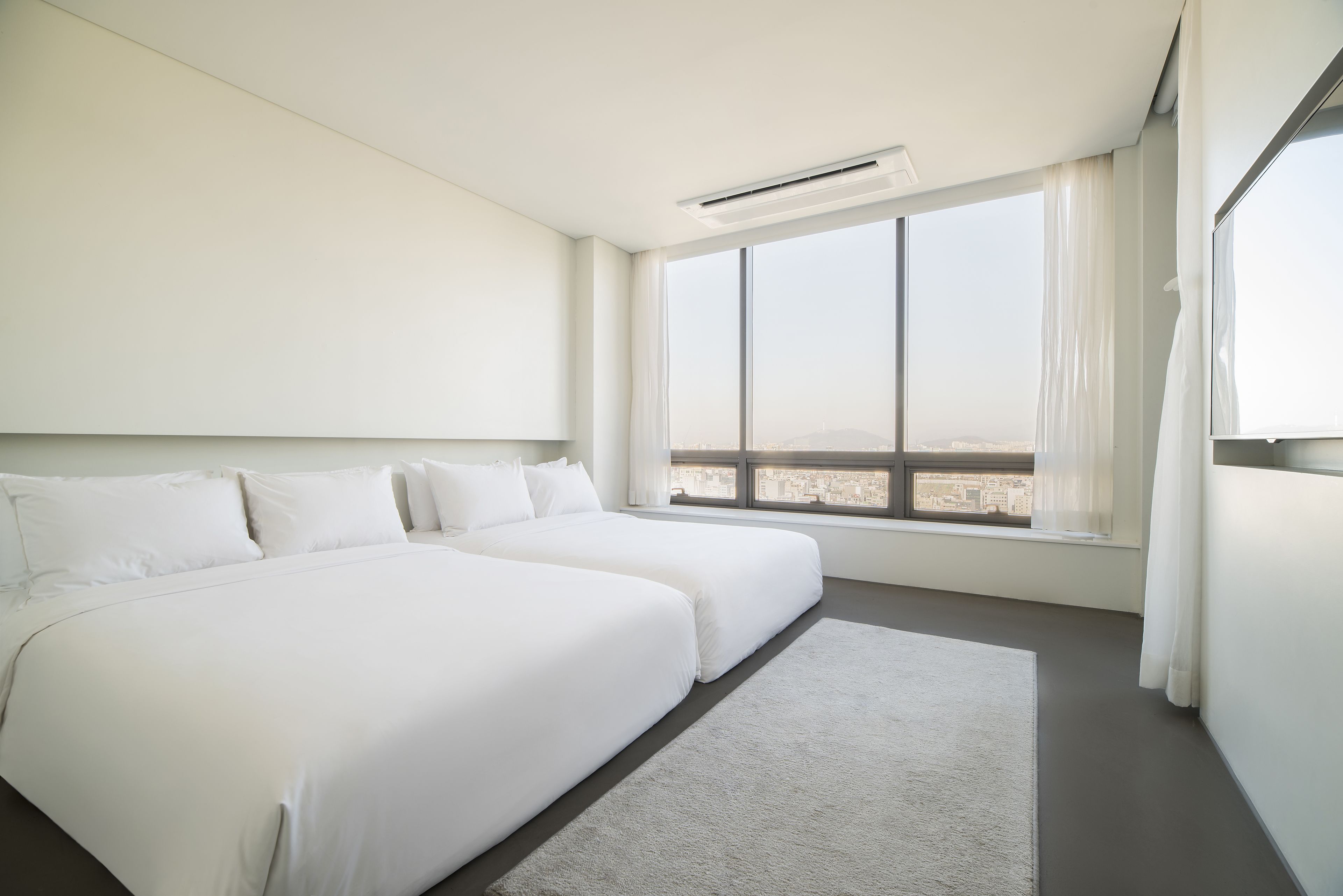 A modern hotel room with a large bed, a view of the city, and a window with curtains.