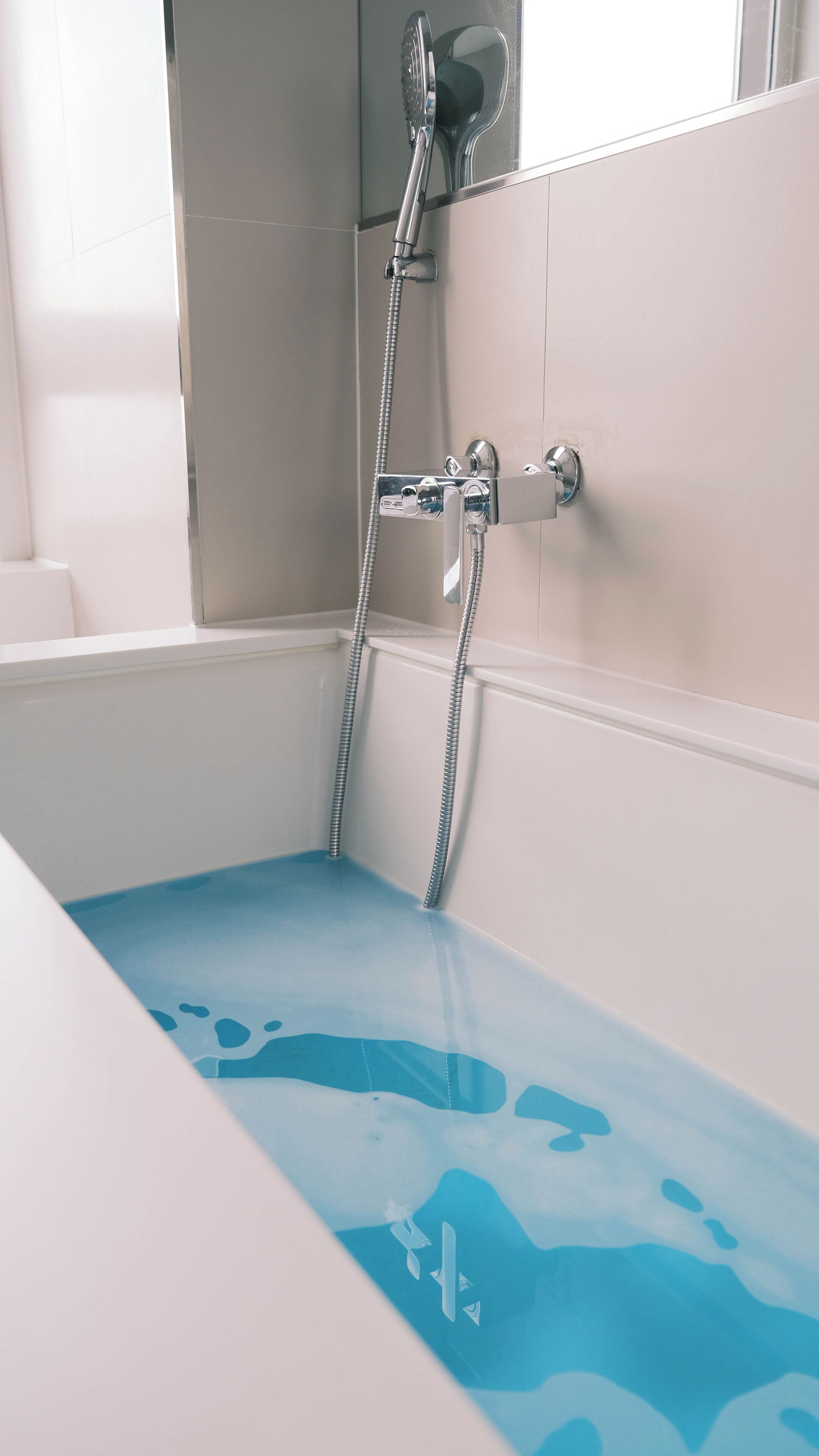 Un baño con ducha, bañera con un estampado azul y paredes blancas.