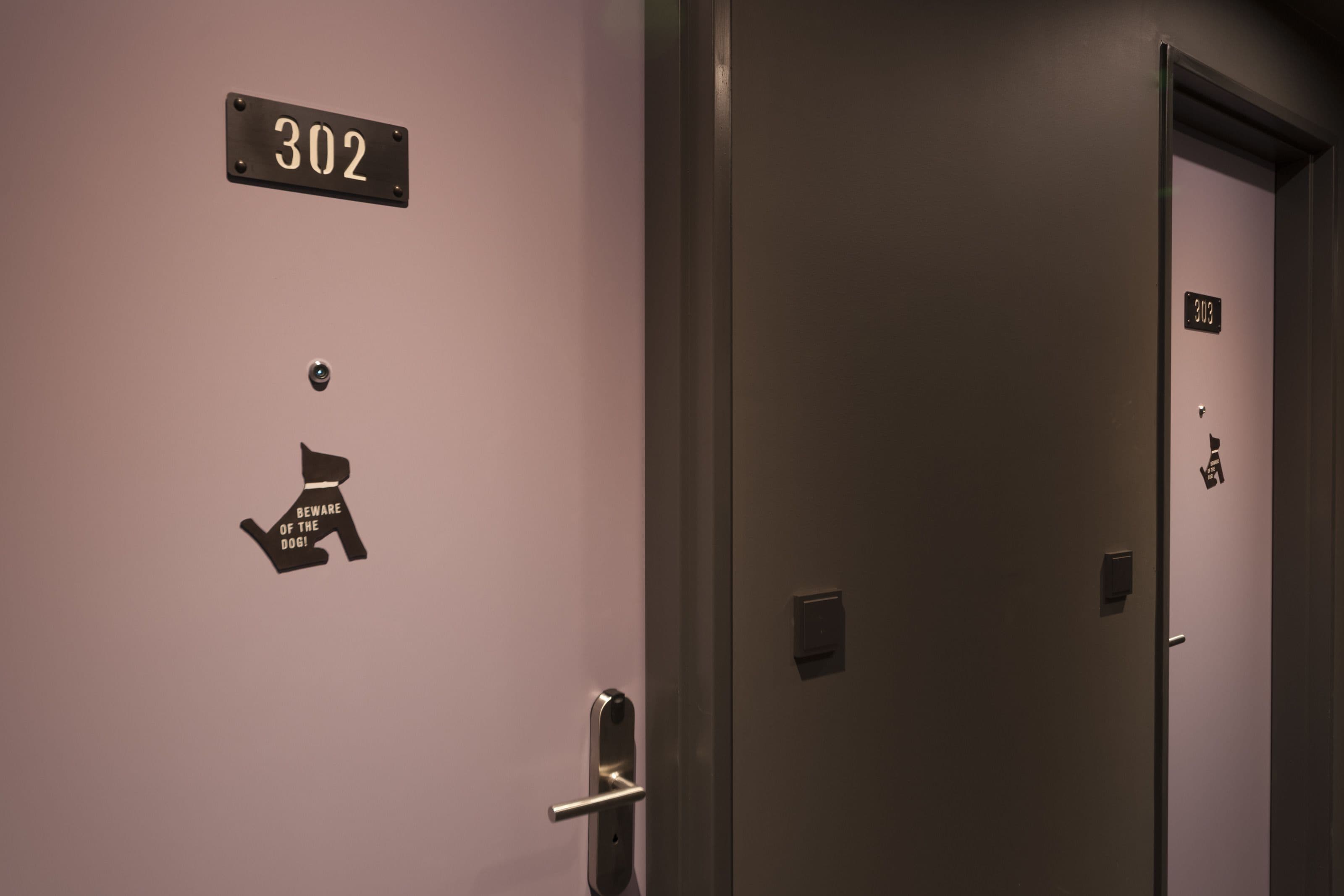 Un pasillo con una puerta marcada con el número 302 y un cartel que dice 'Cuidado, perro'.