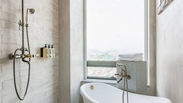 Ein Badezimmer mit einer freistehenden Badewanne, einer Duschbrause und einem Fenster mit Blick auf die Stadt.
