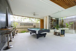 A modern indoor pool area with a pool table, seating, and a television. - Pulau Boutique Villas (Kerobokan)