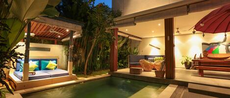 A pool area with a seating area, a covered section, and a dining table with an umbrella.
