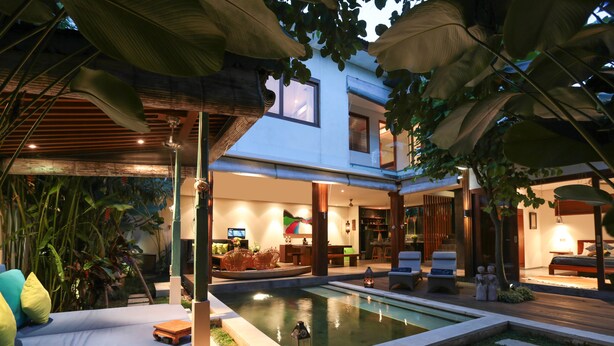 Una casa moderna con piscina, mobiliario exterior y abundante vegetación.
